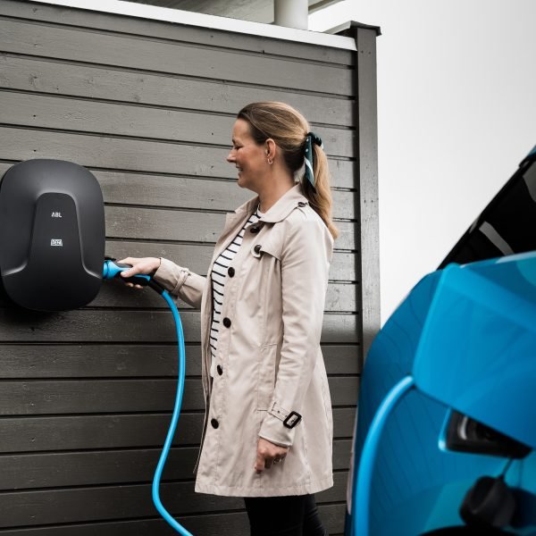 Kvinne lader blå elbil med ladebokks på veggen